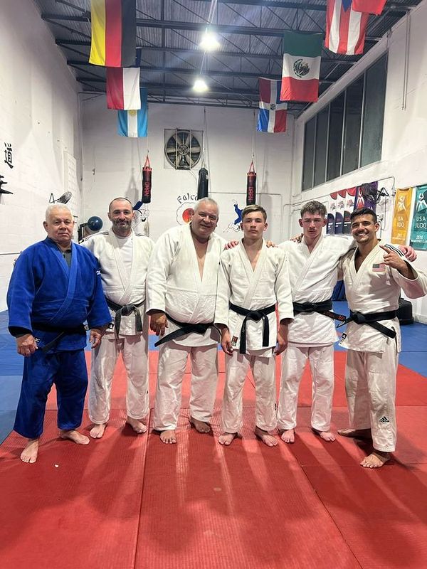 Seven adult judokas lined up in the dojo under the flags.