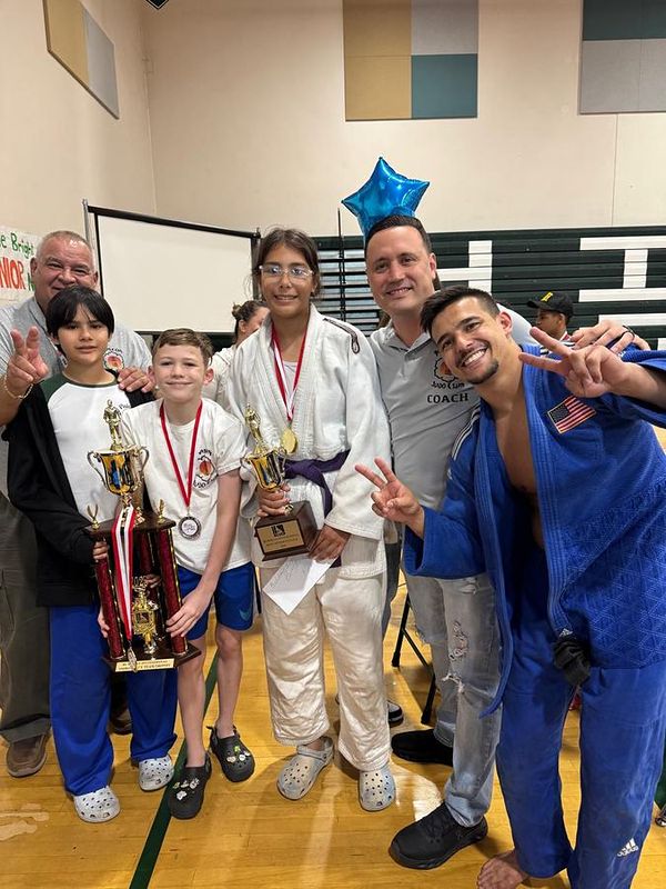 Kids holding trophies and medals next to their coaches at a tournament.