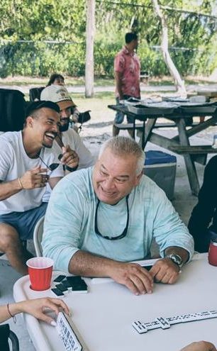 Falcon families laughing around a domino table at an outdoor gathering.